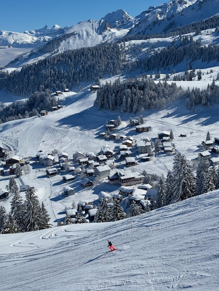 A skier descends a snowy slope in Morschach, Switzerland with stunning mountain views.